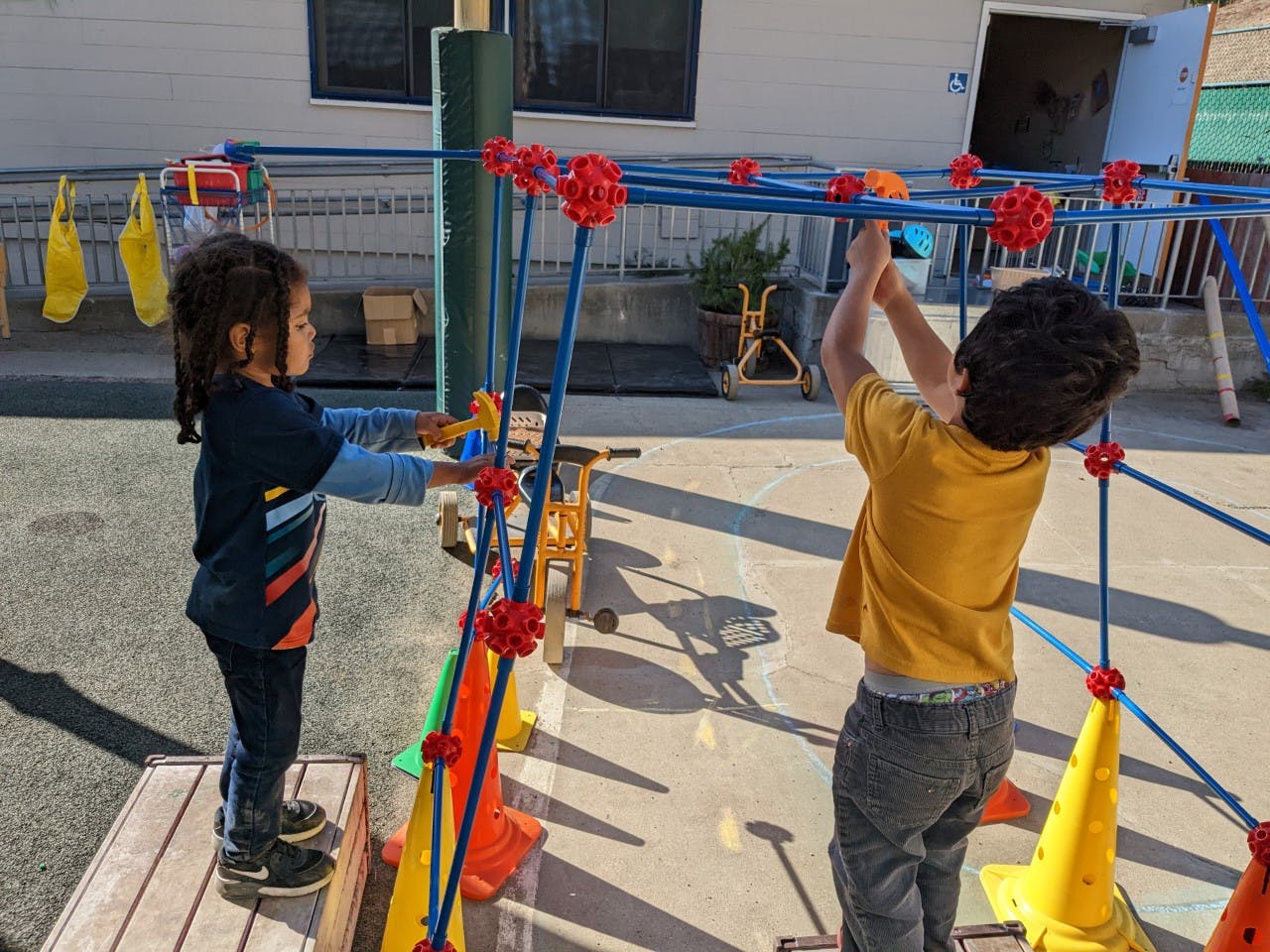 Two children playing with a blue and red construction toy outdoors