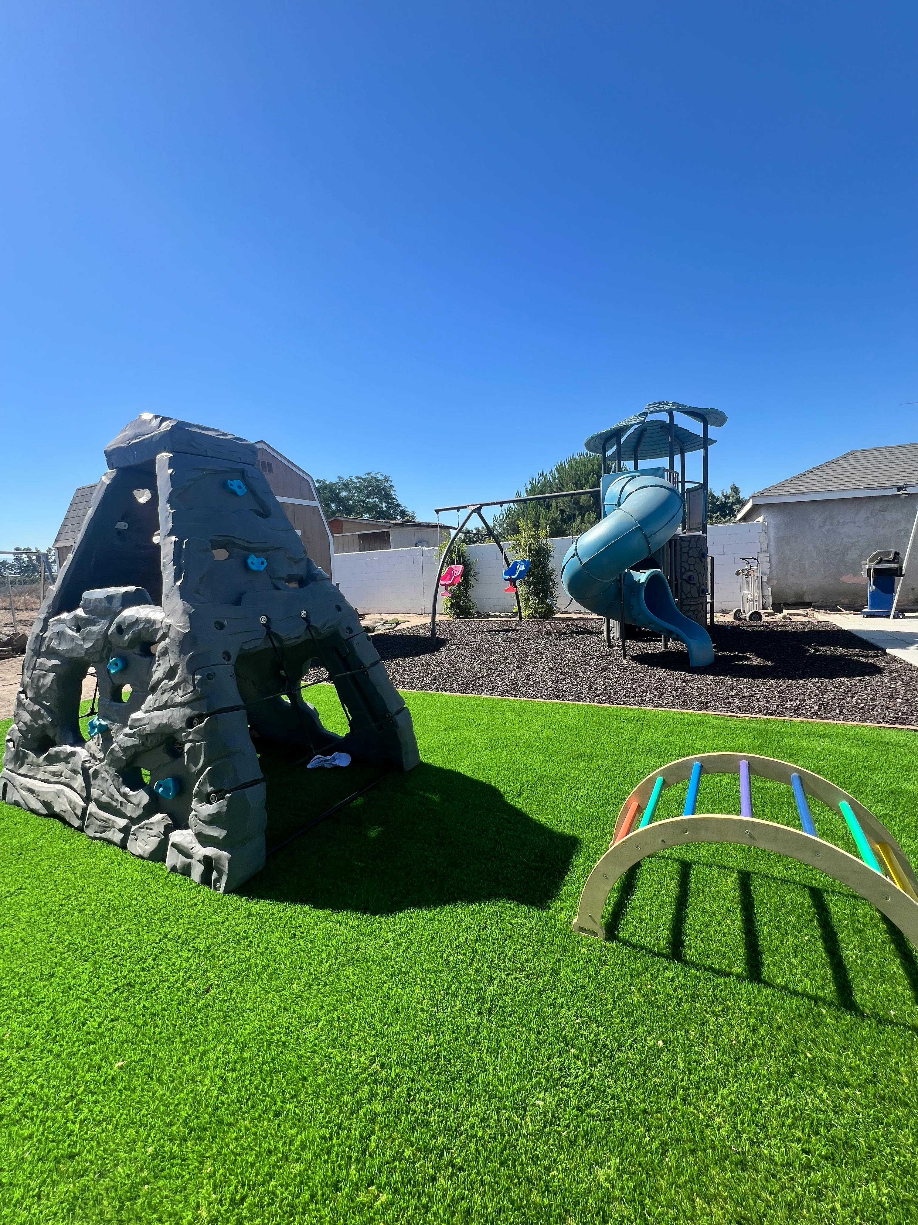 Playground with a climbing structure, slide, and swings on artificial turf