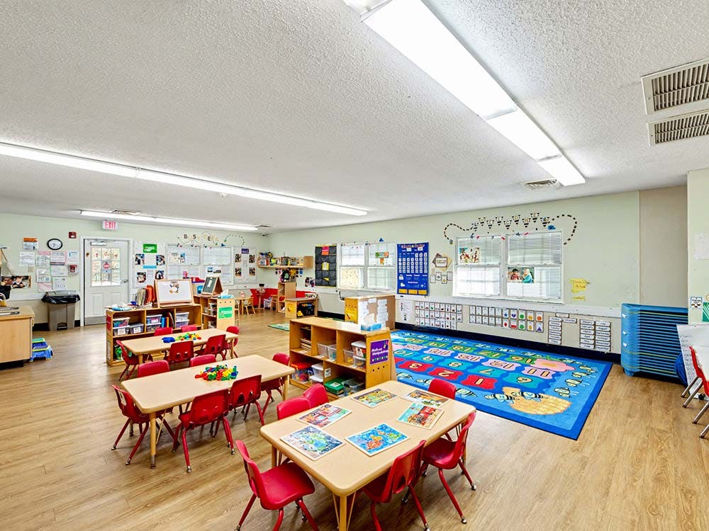 Empty classroom with small tables and red chairs, colorful rug on the floor