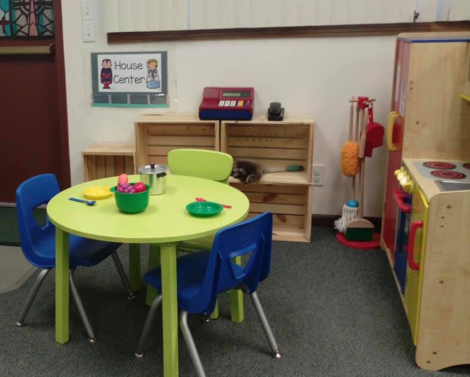 Playroom with a small green table and blue chairs, toy kitchen, and shelves