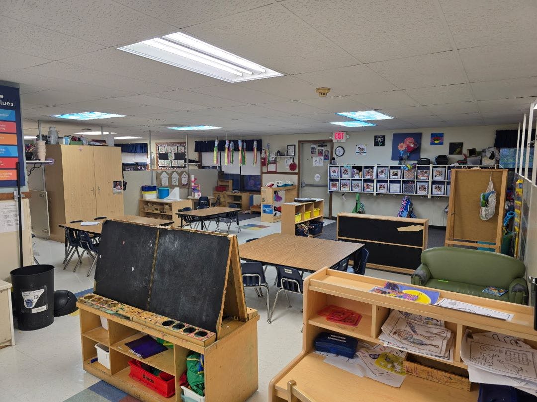 An empty classroom with small tables and chairs, an easel, and cubbies