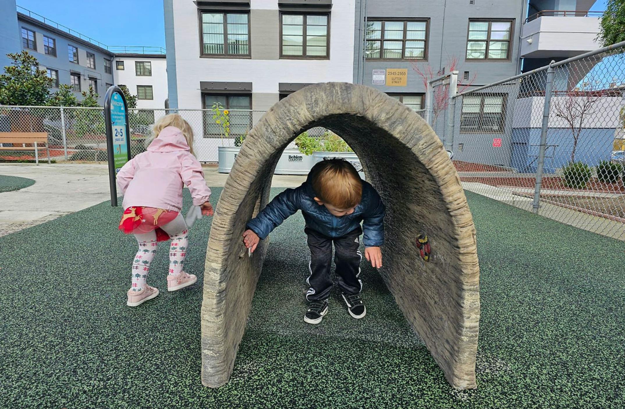 Two children playing on a playground, one crawling through a tunnel