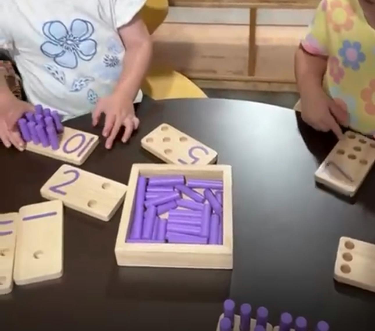 Two children playing with wooden number blocks and purple counting sticks