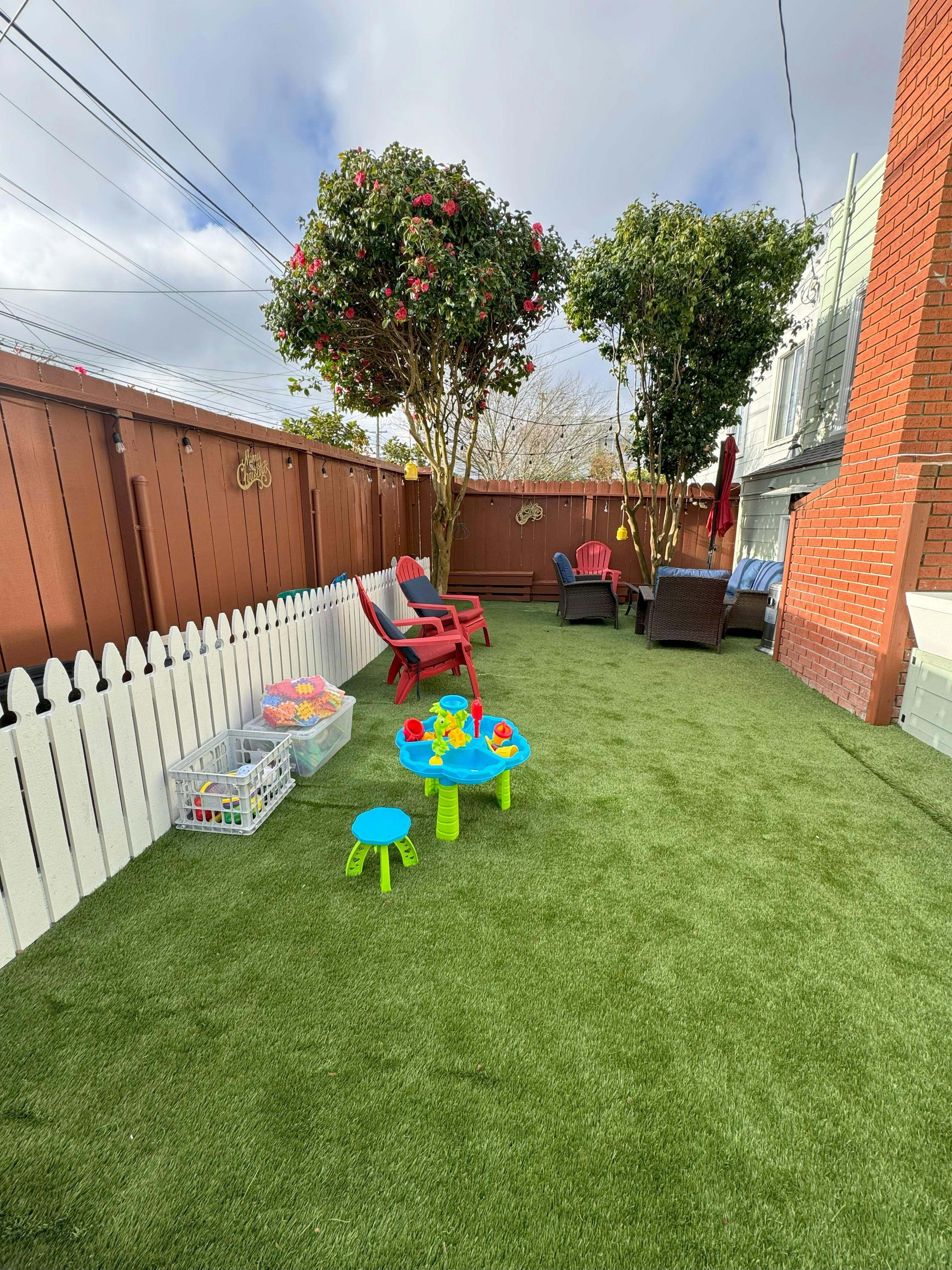 Backyard with artificial turf, white picket fence, and patio furniture