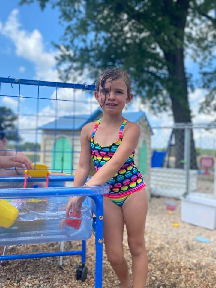 Child in a colorful swimsuit standing next to a water table