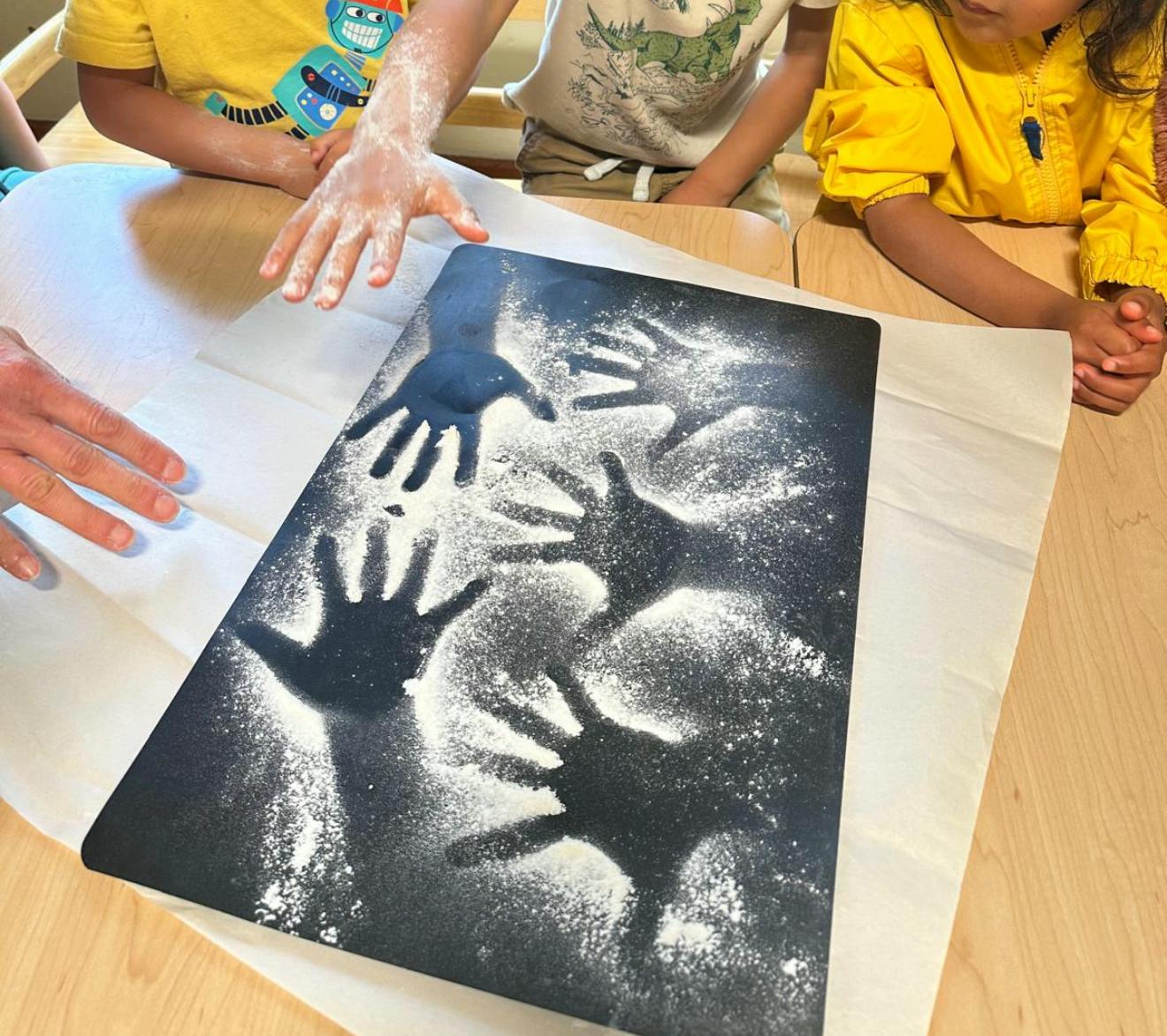 People pressing hands into flour on a black surface to make prints