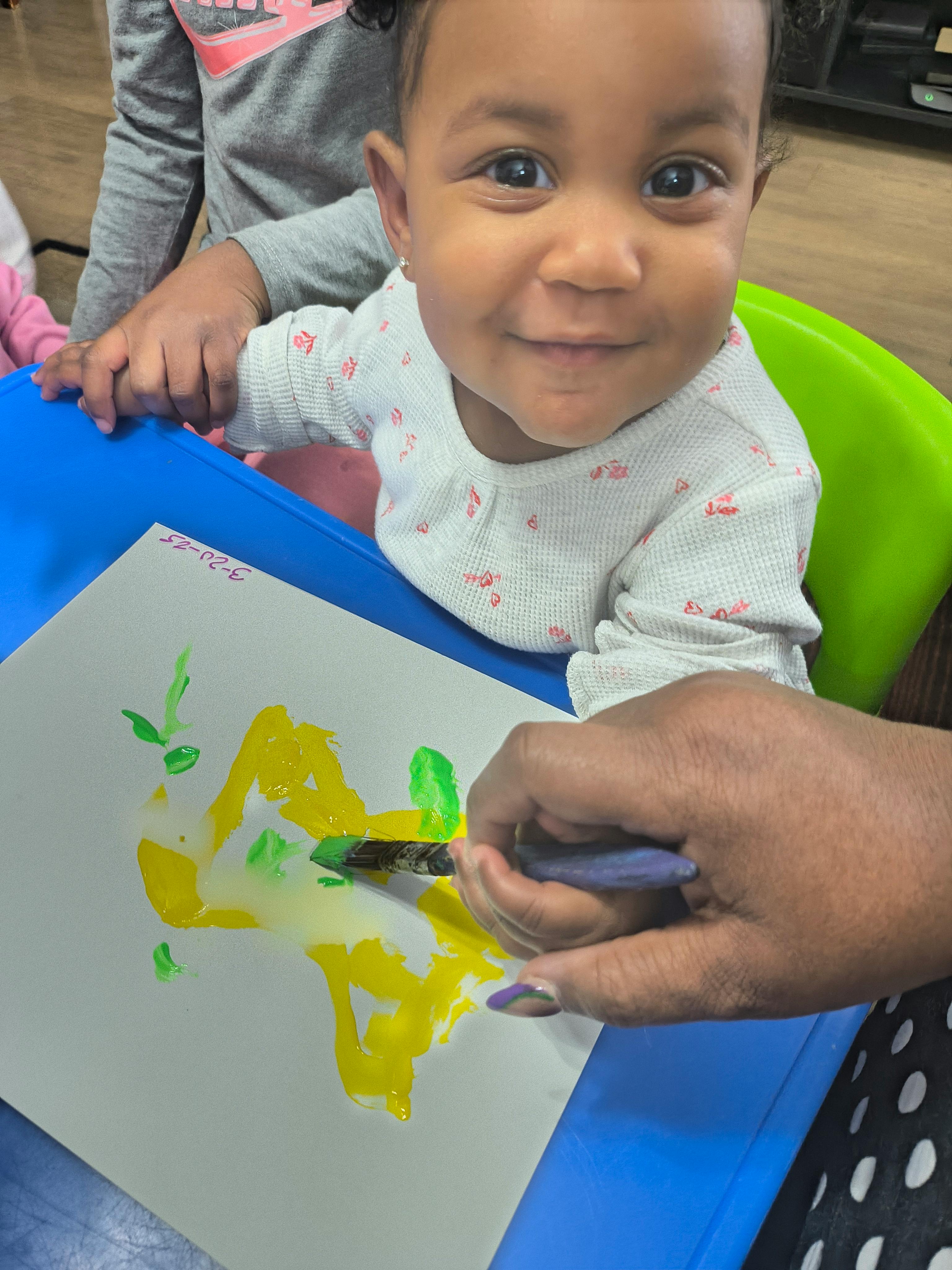 Child painting on paper with a person's hand guiding the brush