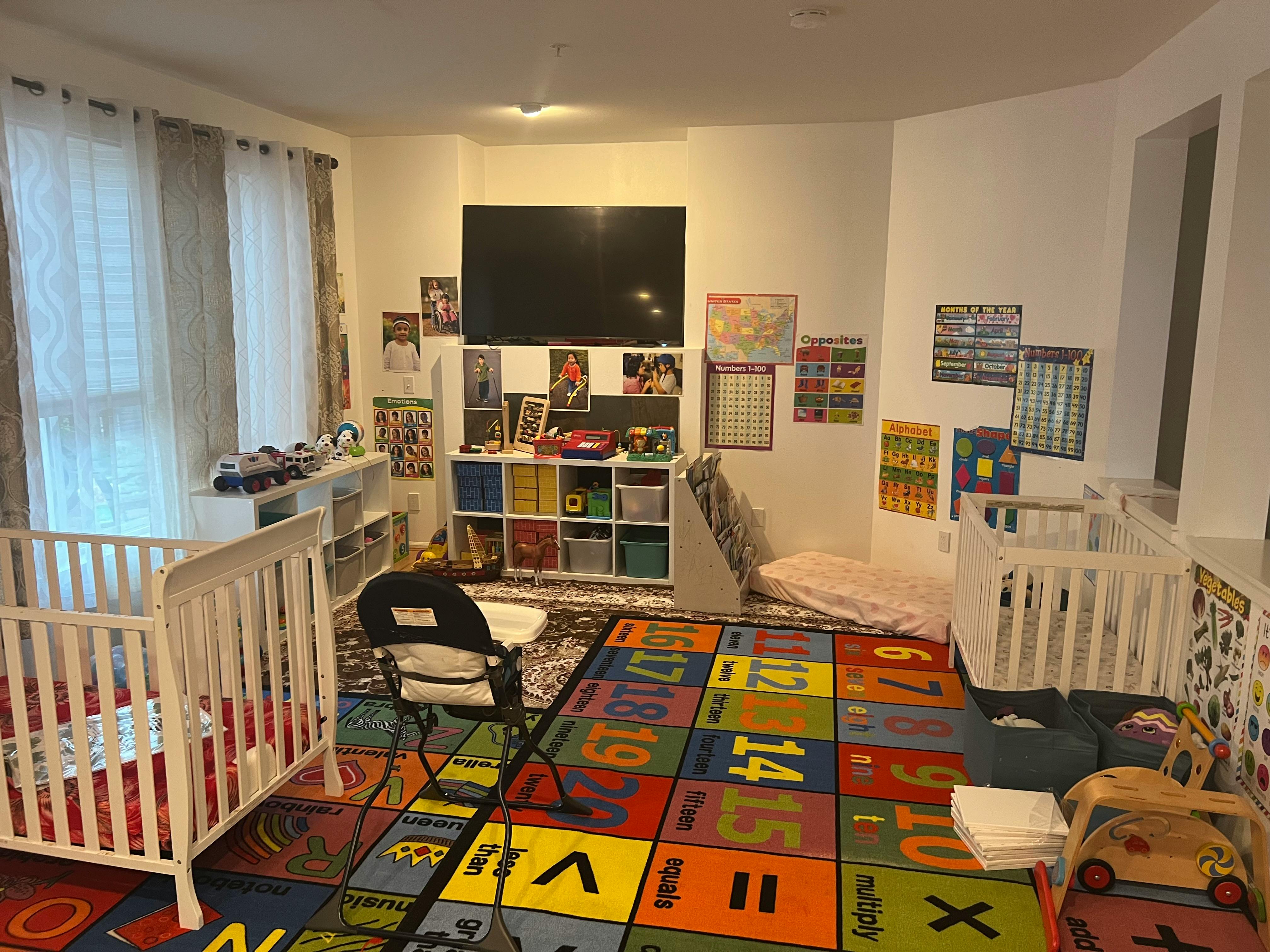 Nursery room with two cribs, a colorful alphabet rug, and a television