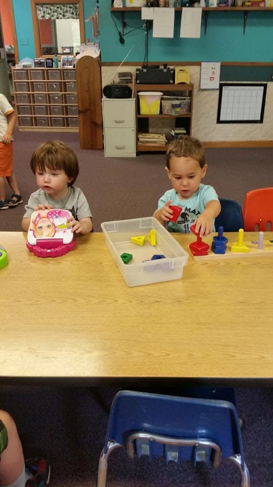 Two children playing with toys at a table in a classroom