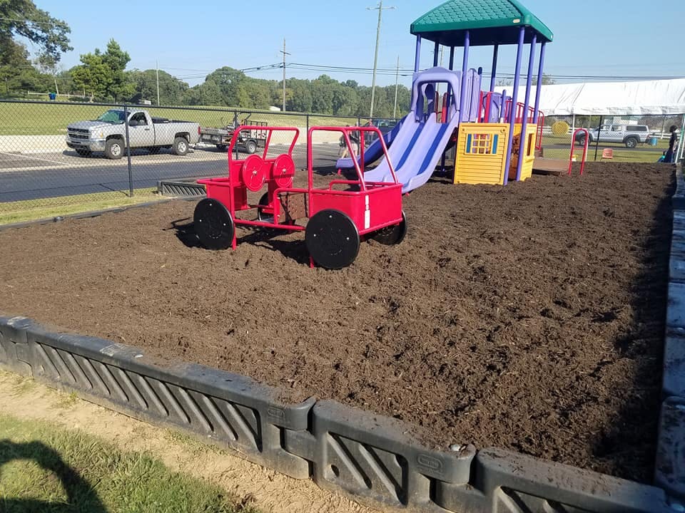 Red playground vehicle and purple slide on wood chips