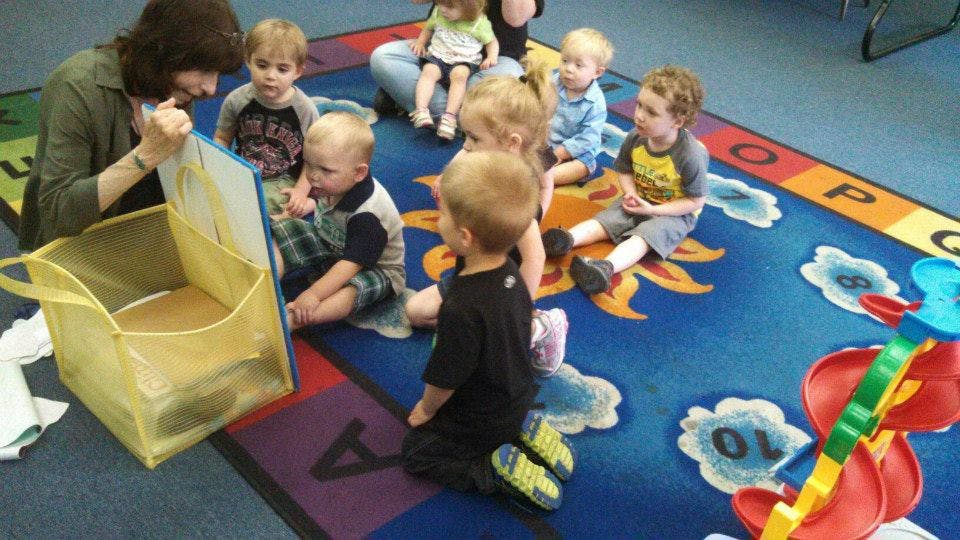 Adult showing a book to children sitting on a rug
