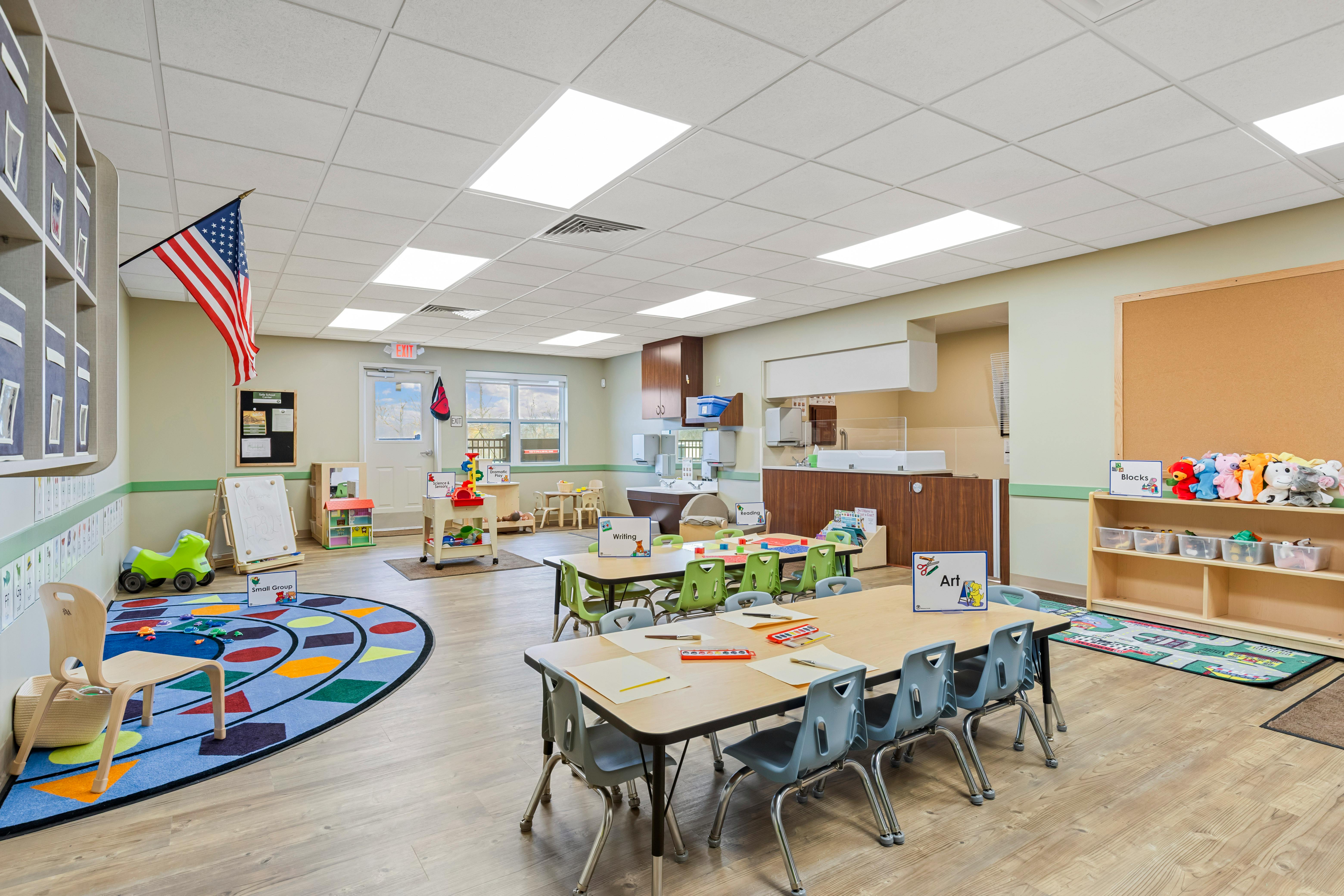 Classroom with small tables, chairs, colorful rugs, and play areas