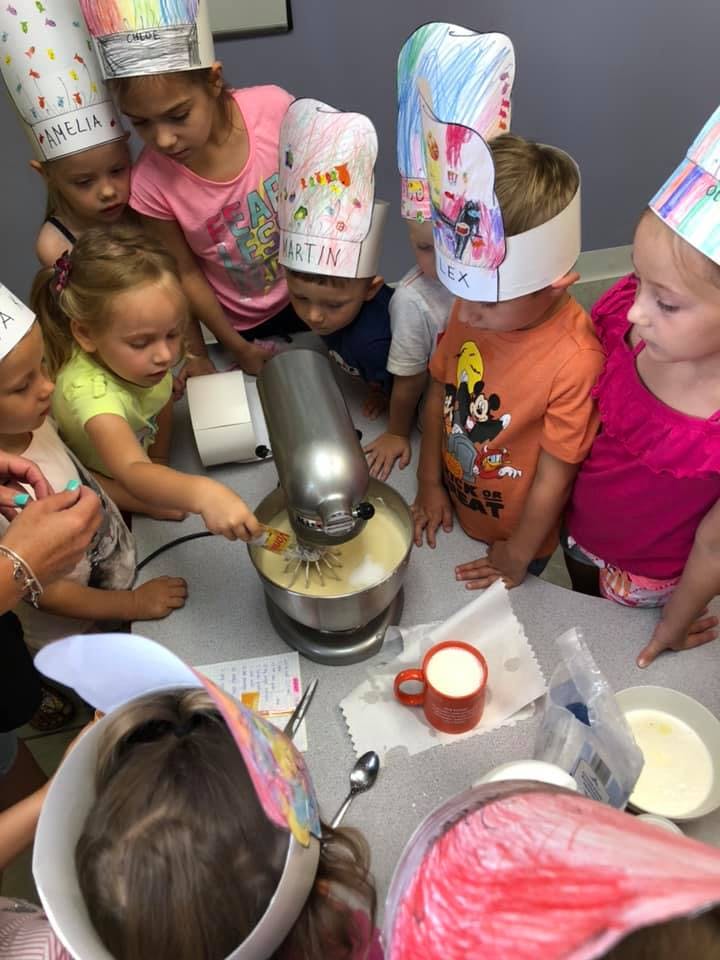Children in chef hats gathered around a stand mixer, one child stirring the bowl