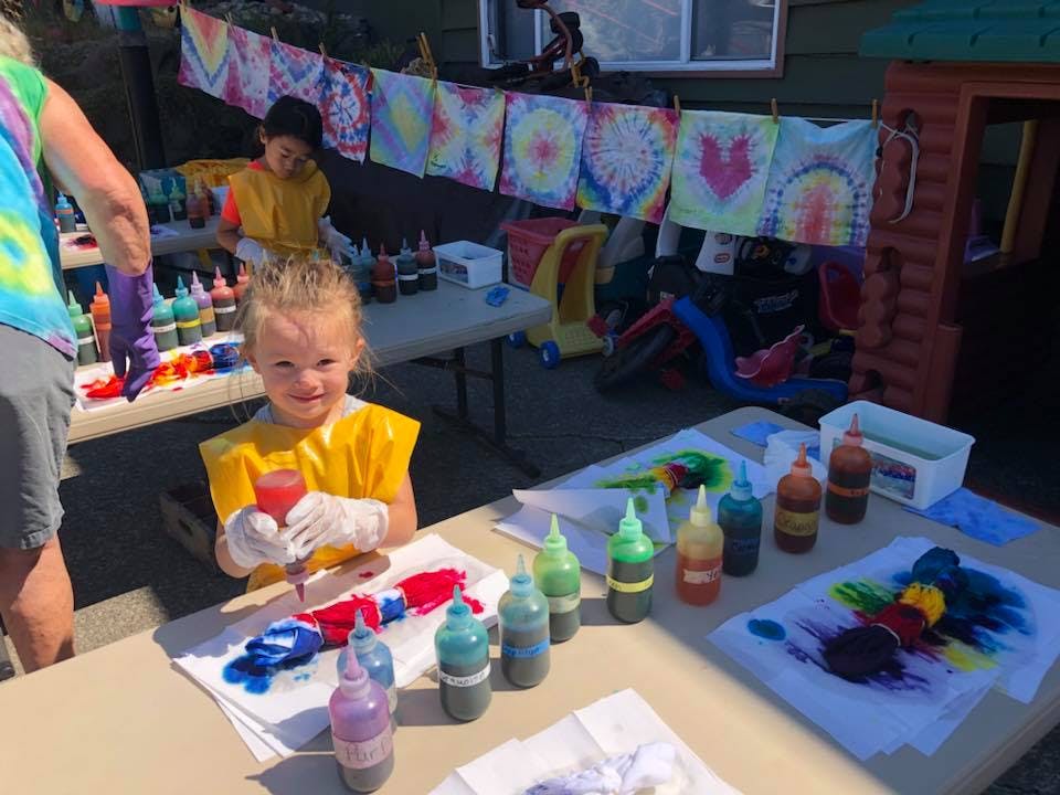 Child in yellow smock tie-dyeing a shirt at a table