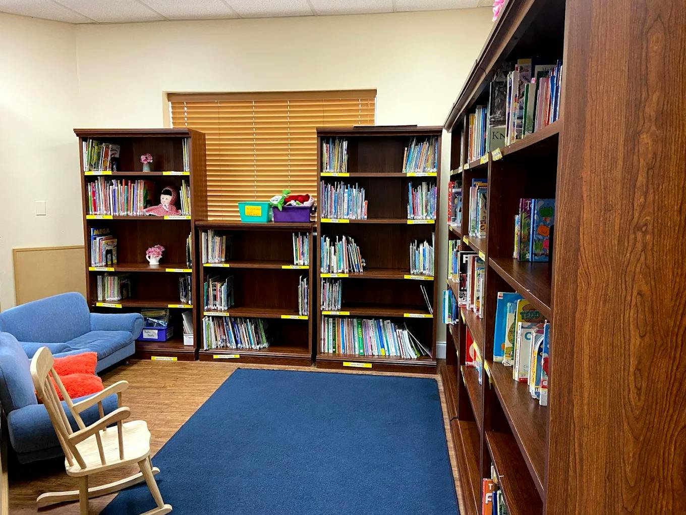 Library room with bookshelves, blue sofas, and a wooden rocking chair