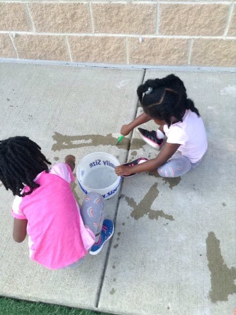 Two children playing with water and a bucket on concrete