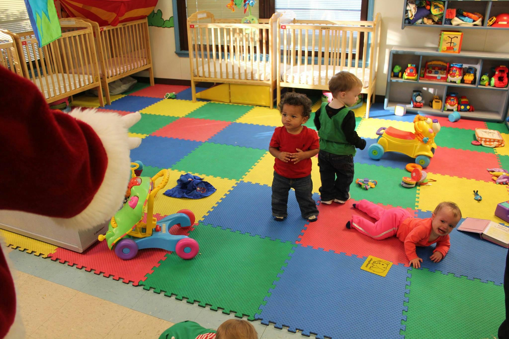 Children playing on a colorful mat in a room with cribs