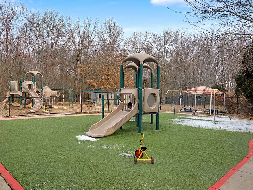Playground with multiple slides, swings, and a small tricycle on artificial grass