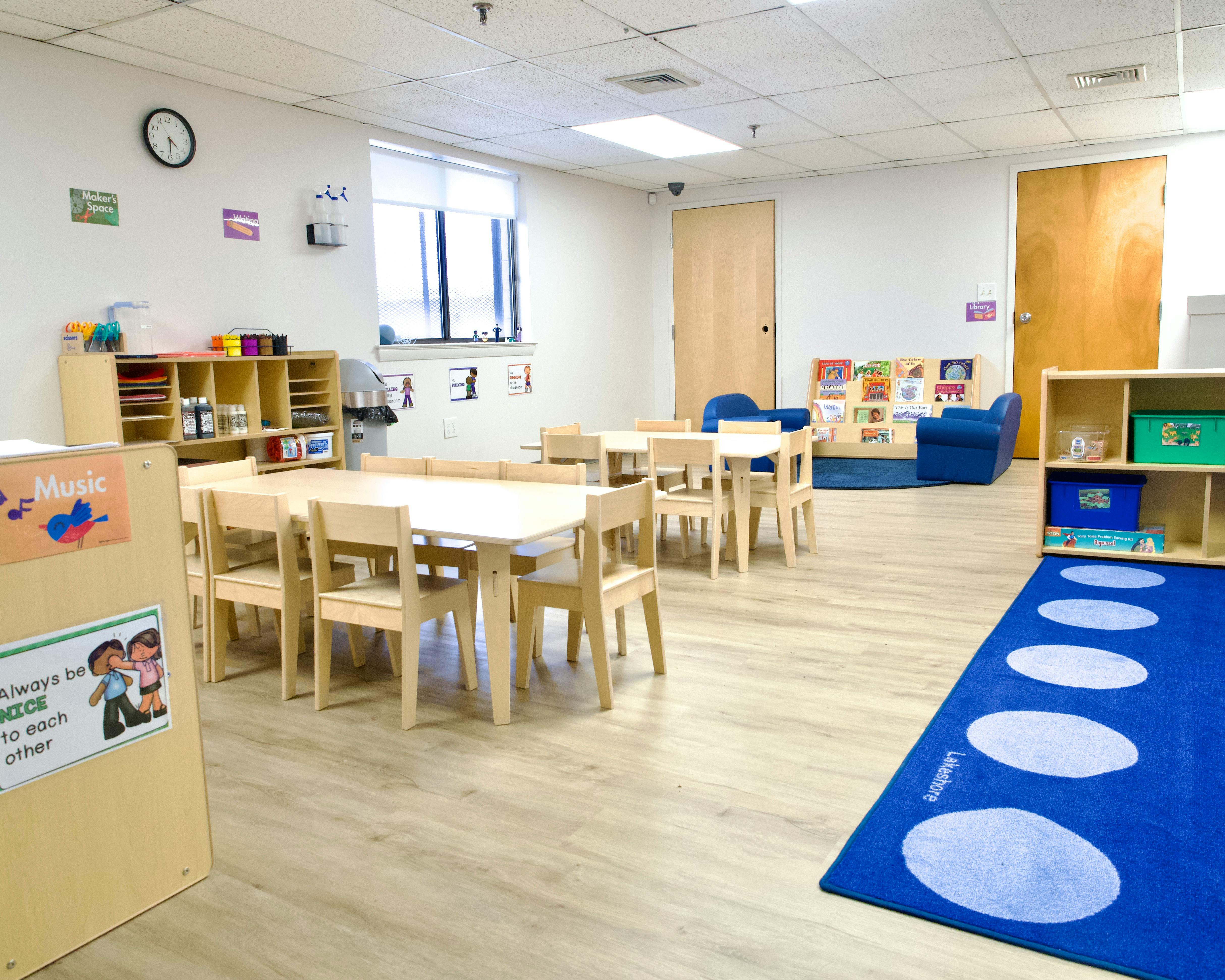 Classroom with small tables and chairs, blue rug, and shelves