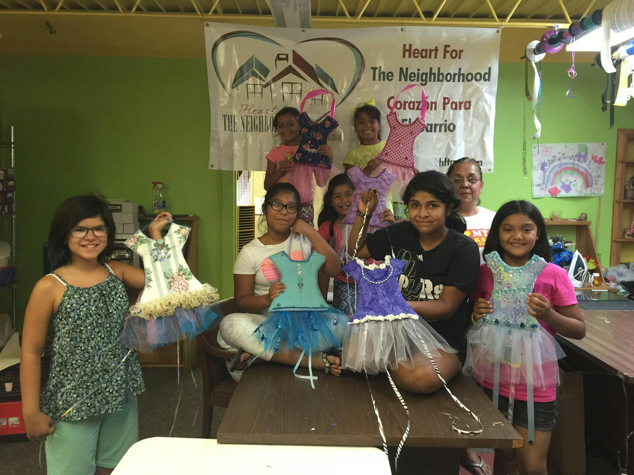 Group of people and children holding up small decorative dresses