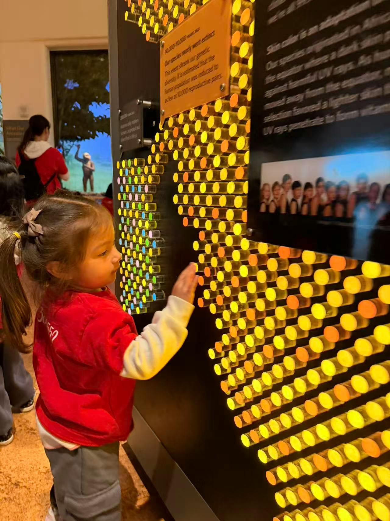 Child in a red shirt touching a lighted display with yellow and orange circles