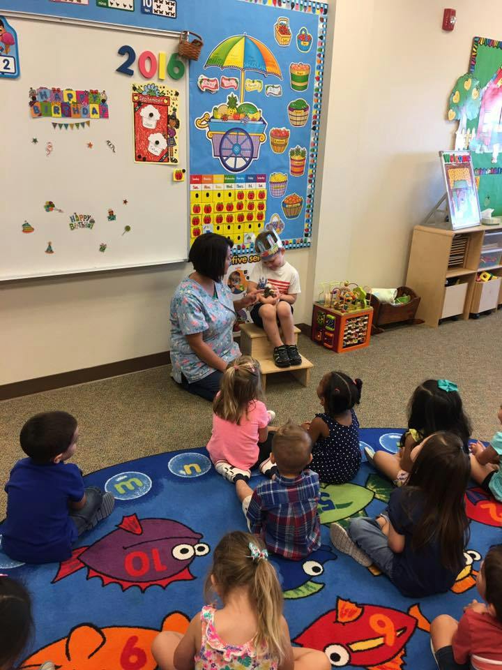 Adult reading to a child on a stool with other children sitting on a rug