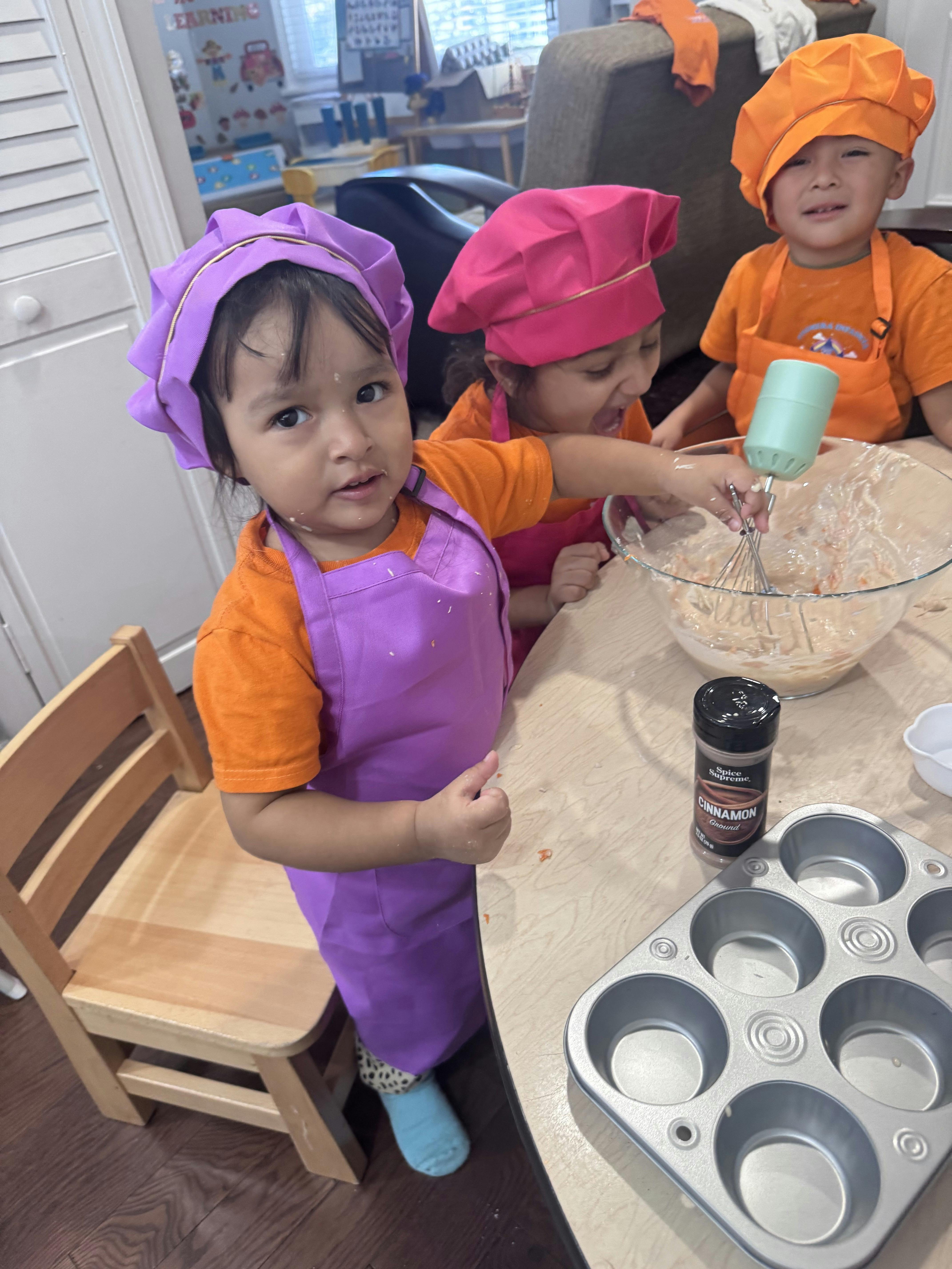 Three children in chef hats and aprons mixing batter in a bowl