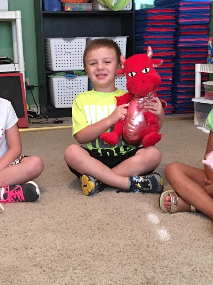 Child sitting on floor holding a red dragon stuffed animal