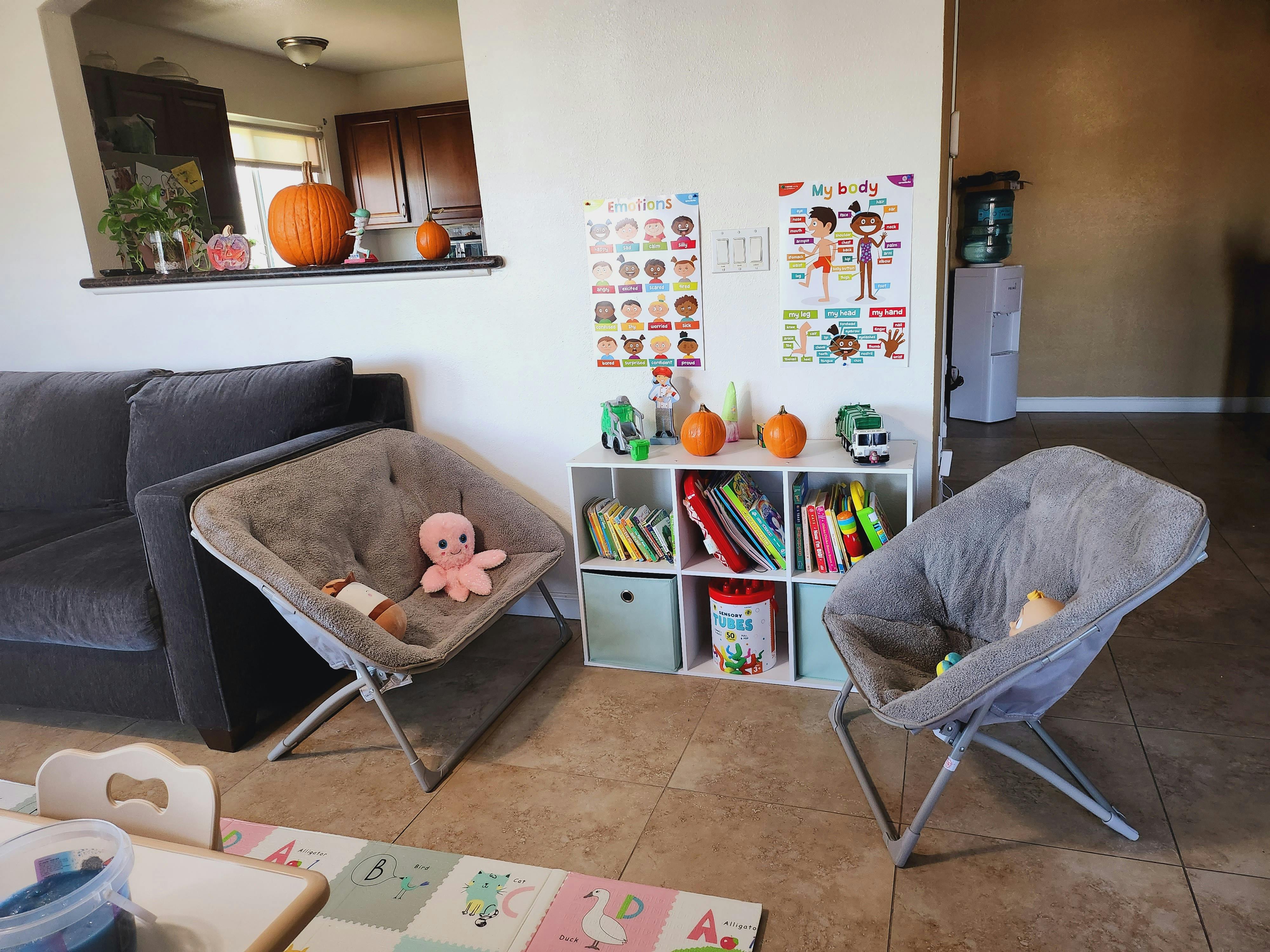 Living room with two gray chairs, a sofa, and a white storage shelf with books