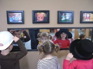 Three children trying on hats in front of a mirror