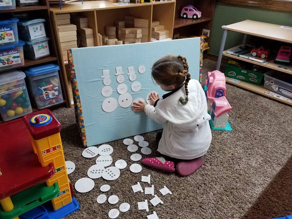 Child kneeling and placing white circles on a blue board