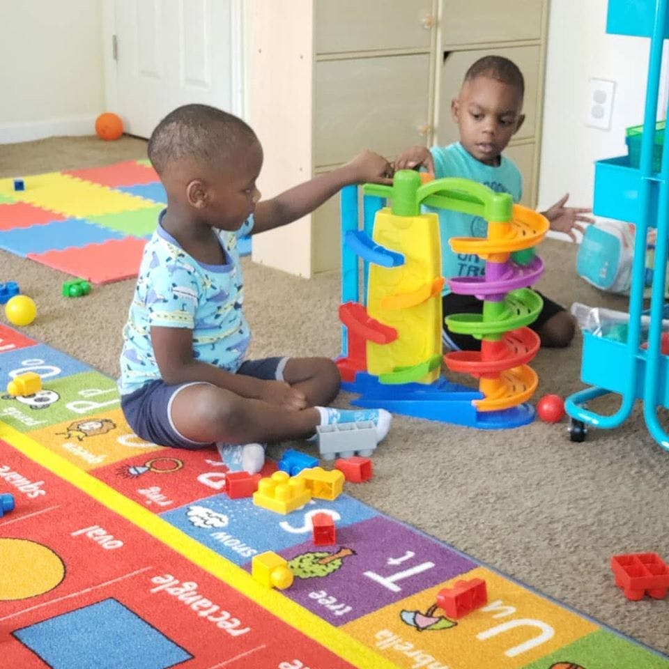 Two children playing with a colorful toy ramp on the floor