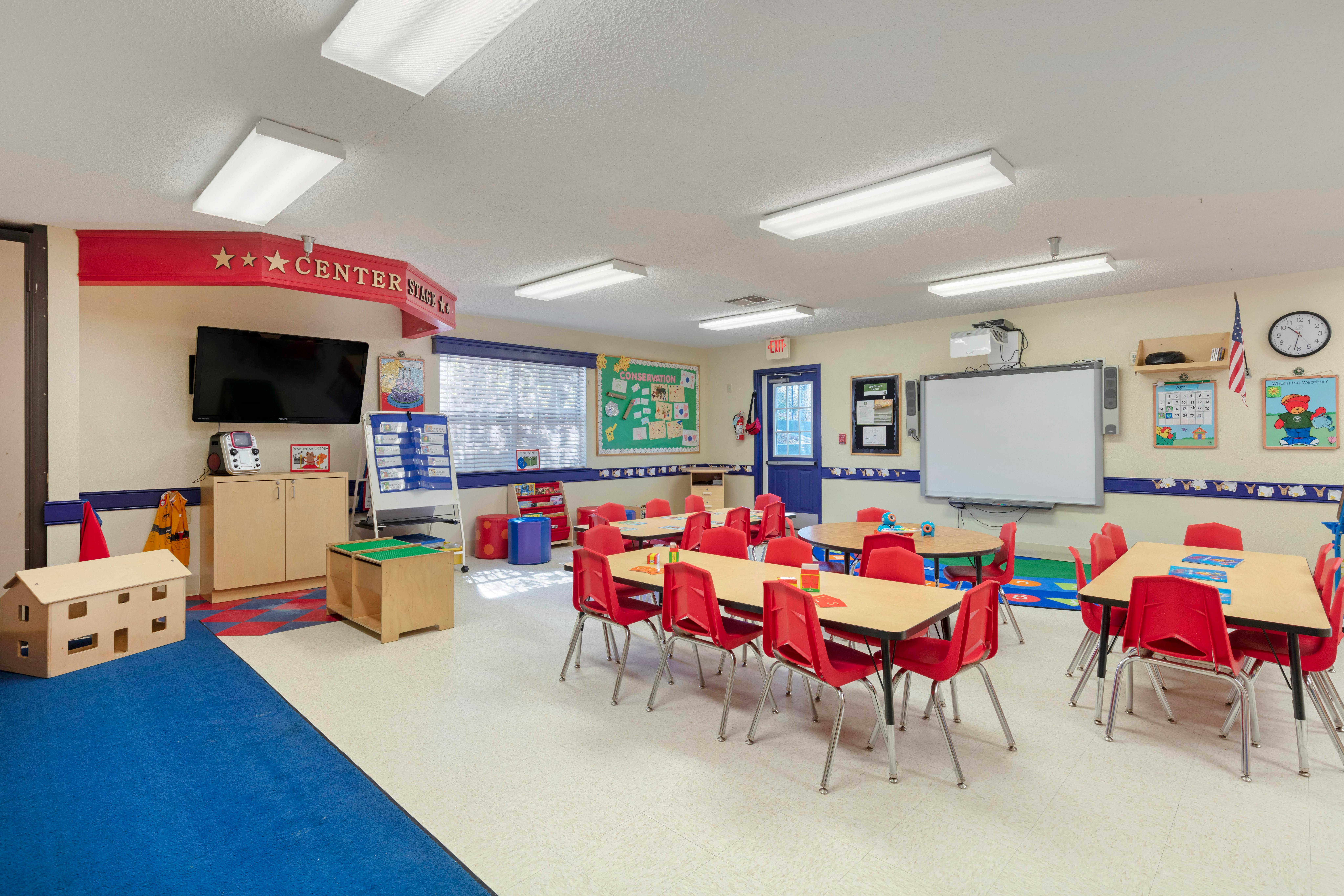 An empty children's classroom with red tables and chairs