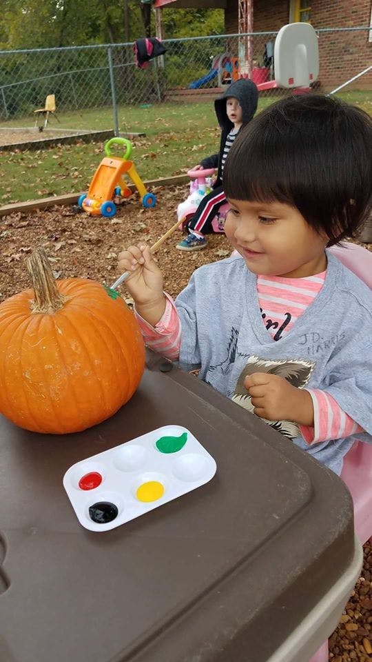 Child painting a pumpkin at a table outdoors