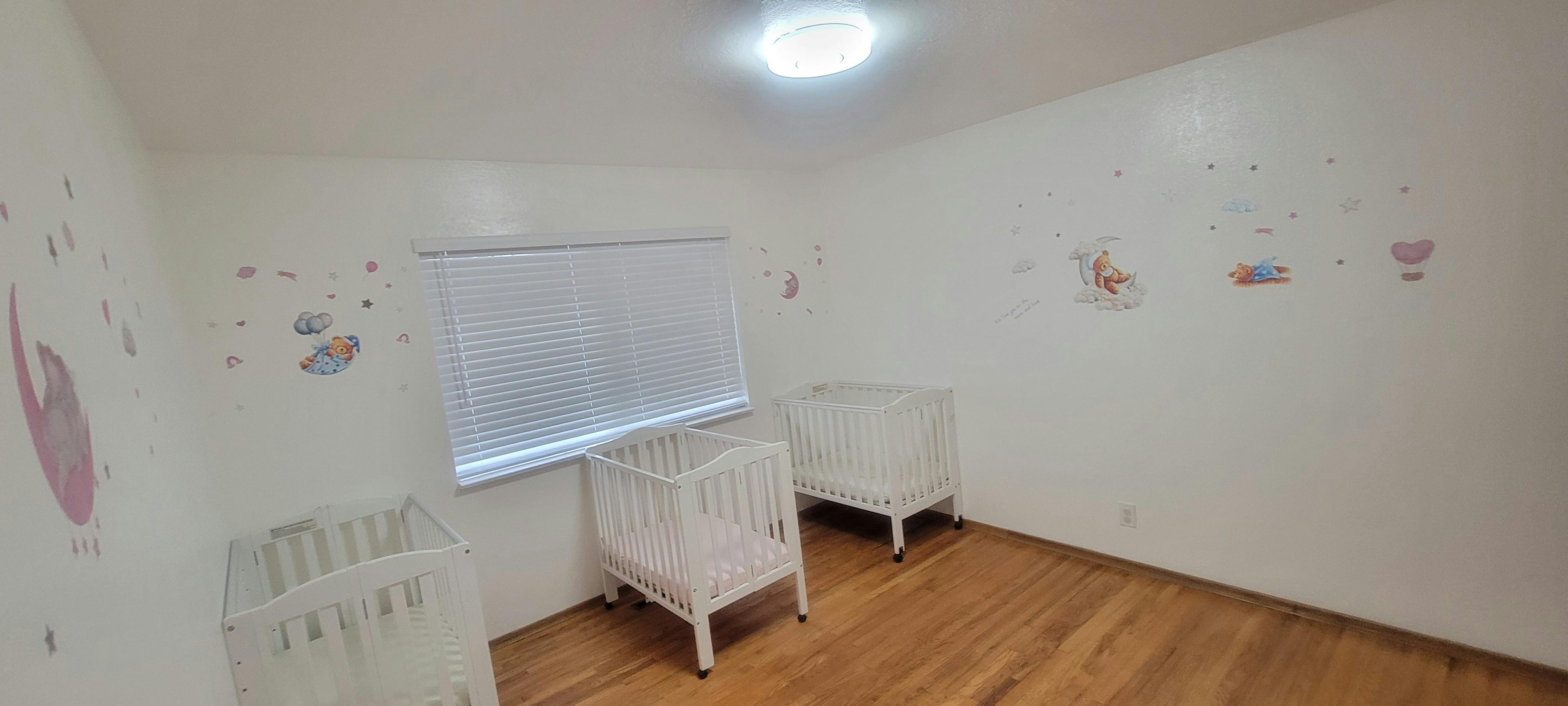 Empty room with three white cribs and wall decals
