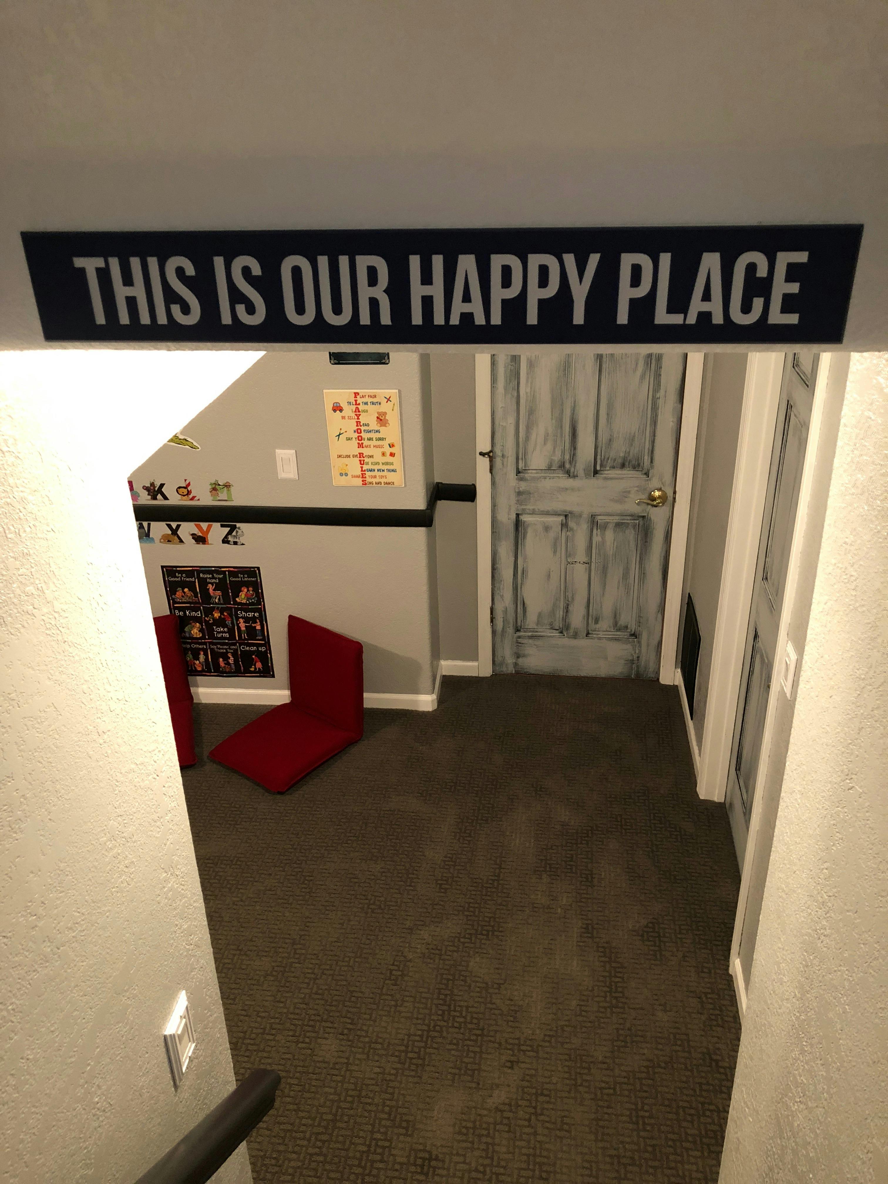 Sign reading "THIS IS OUR HAPPY PLACE" above a carpeted room with a red chair