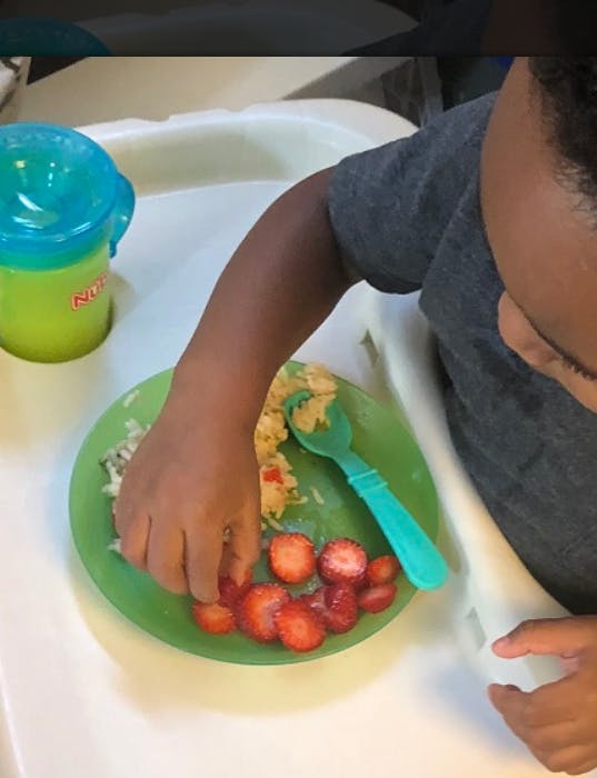 Child in a high chair eating strawberries and other food from a green plate
