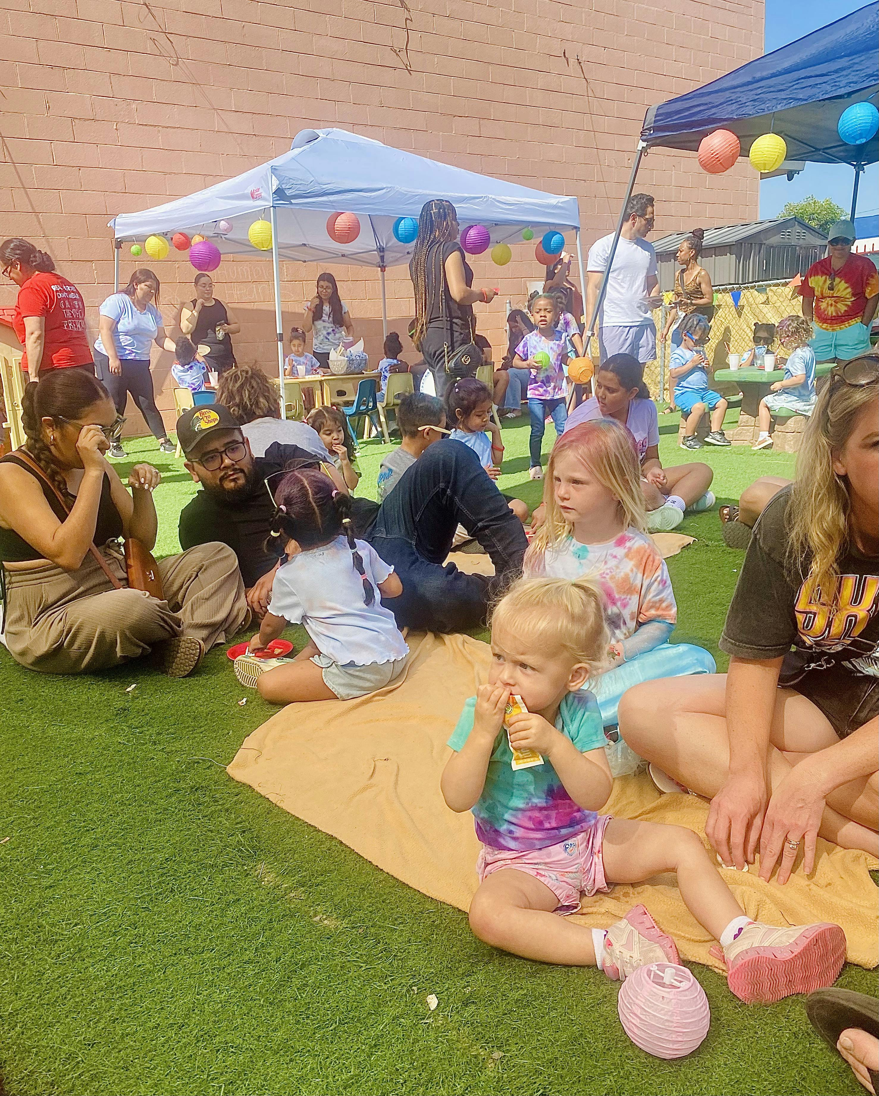 People and children gathered on artificial grass under canopies