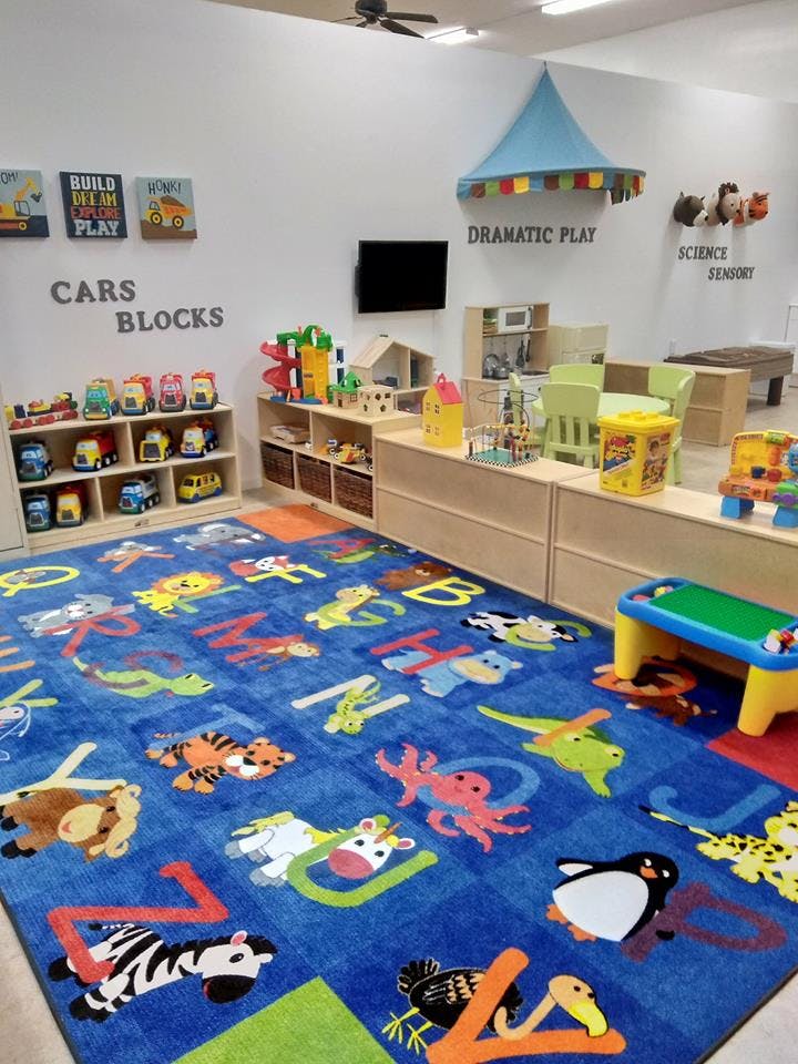 Playroom with a blue alphabet rug, toy shelves, and a dramatic play area