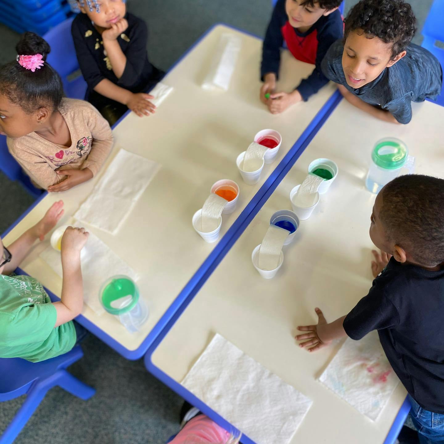 Children at a table with cups of colored liquid