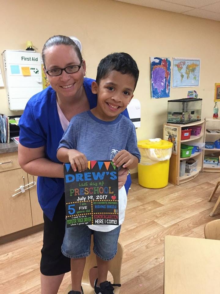 Adult and child holding a sign that reads "Drew's Last Day of Preschool"