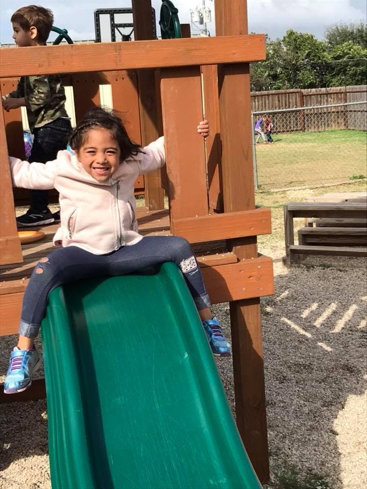 Child sitting at the top of a green slide on a playground