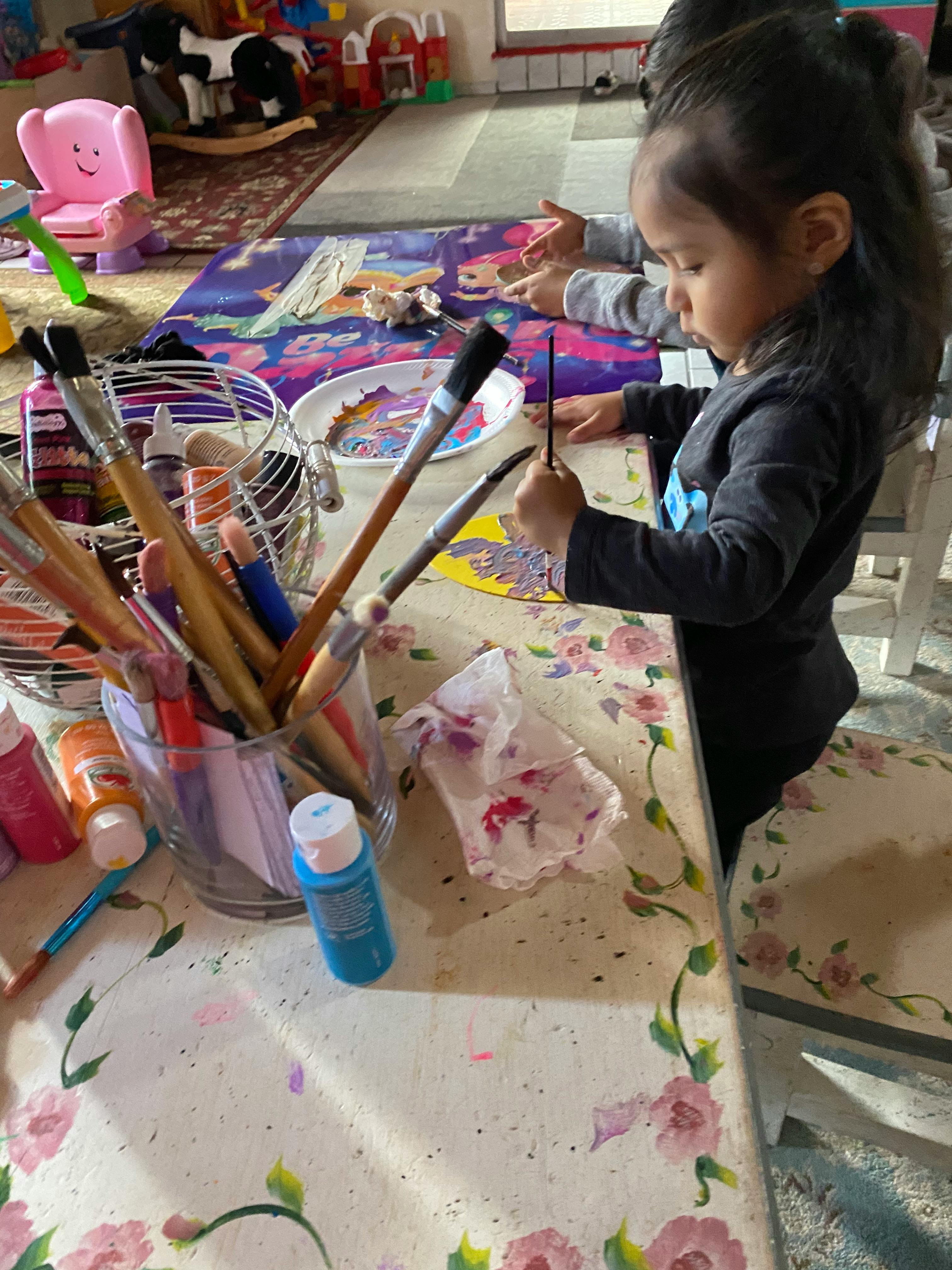 Child painting at a table with paintbrushes and paint bottles