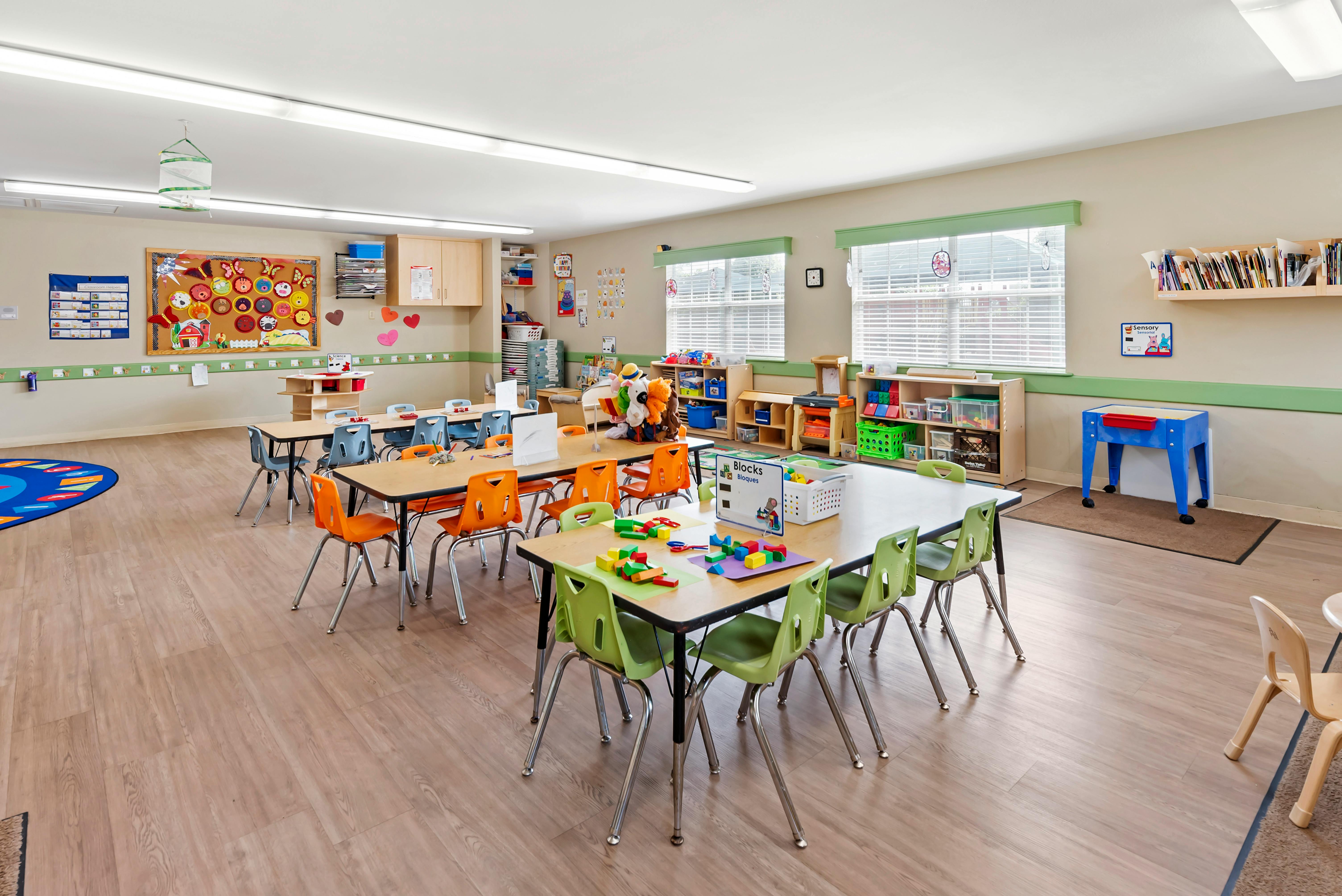 An empty early childhood classroom with multiple tables and chairs arranged