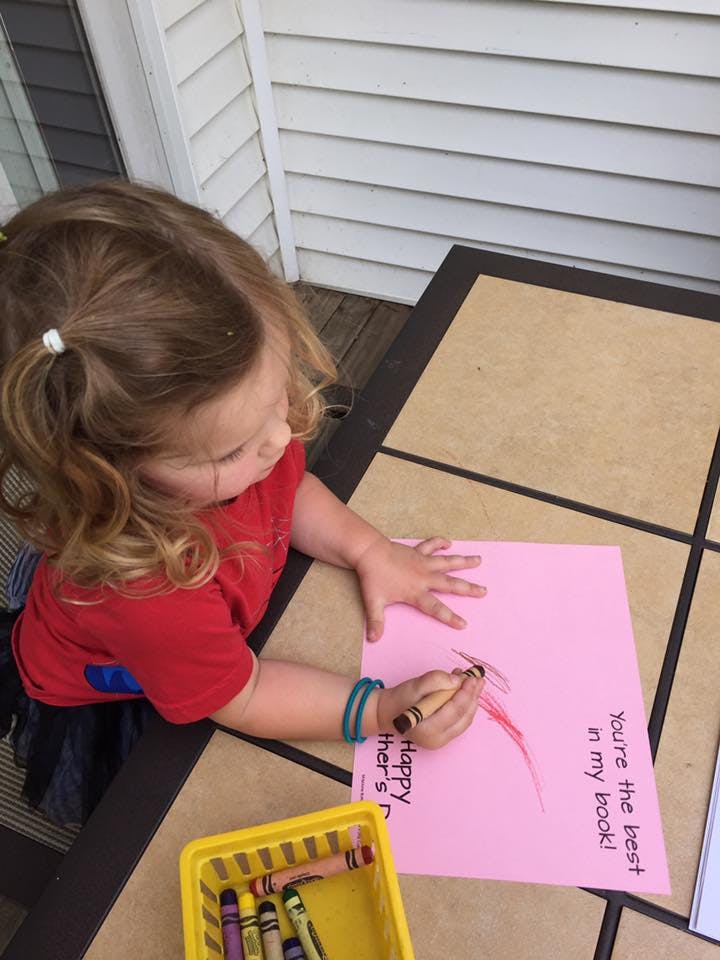 Child drawing on pink paper with a crayon