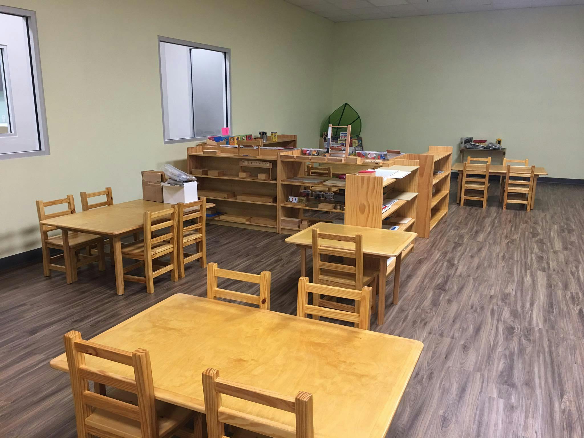 Classroom with small wooden tables, chairs, and shelves