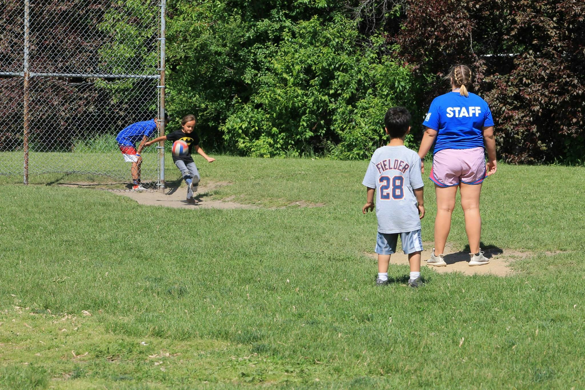 Children and adult playing baseball on a grassy field