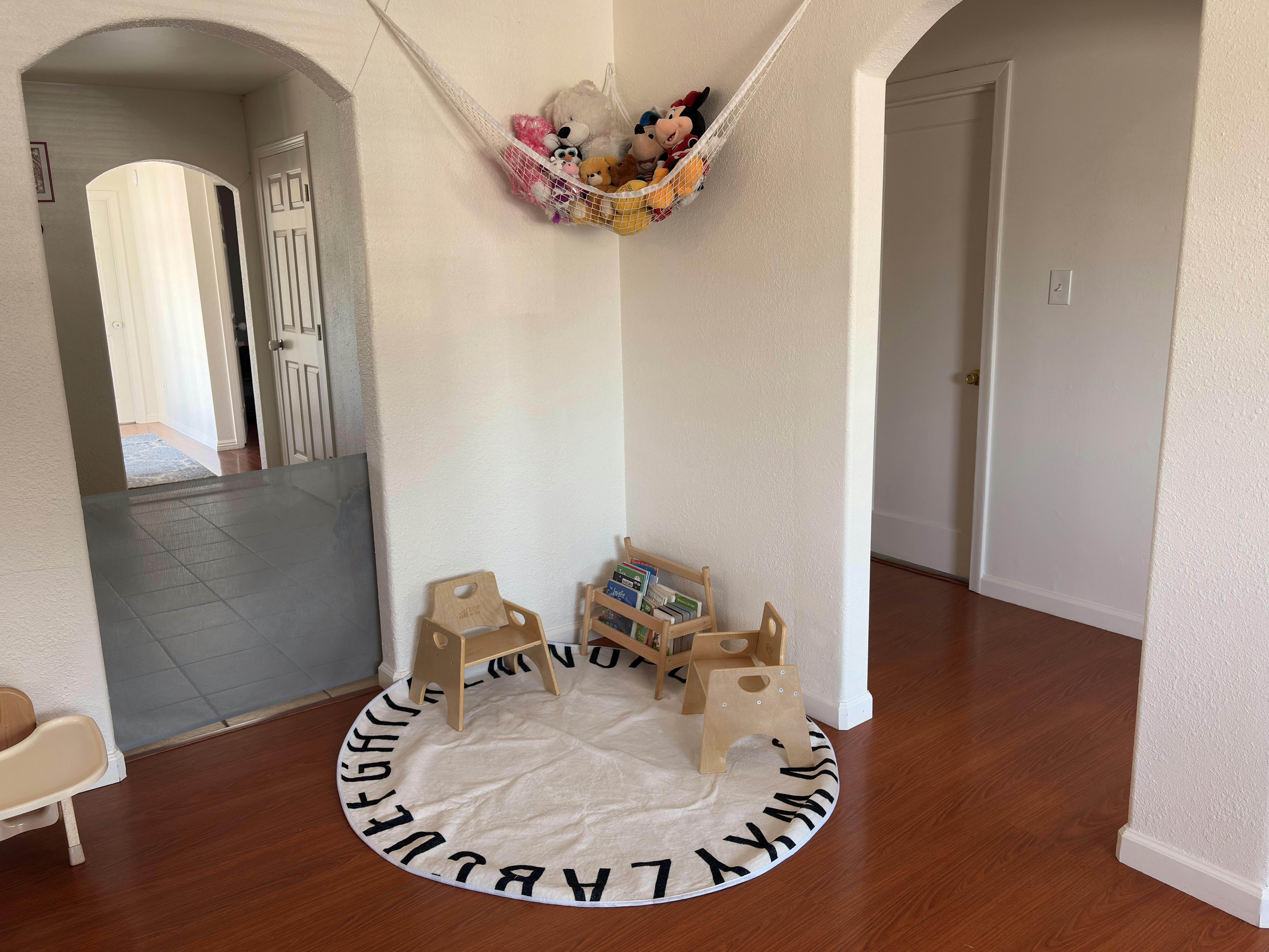 Play area with small wooden chairs, toy shelf, and a round rug with letters