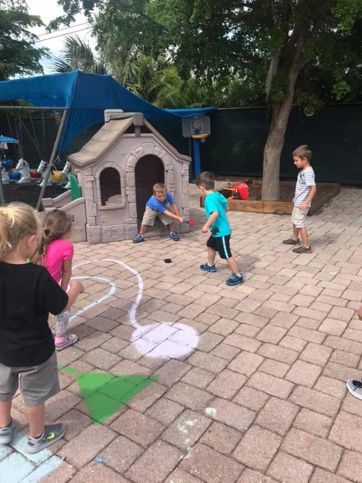 Children playing with hockey sticks and a puck on a paved area