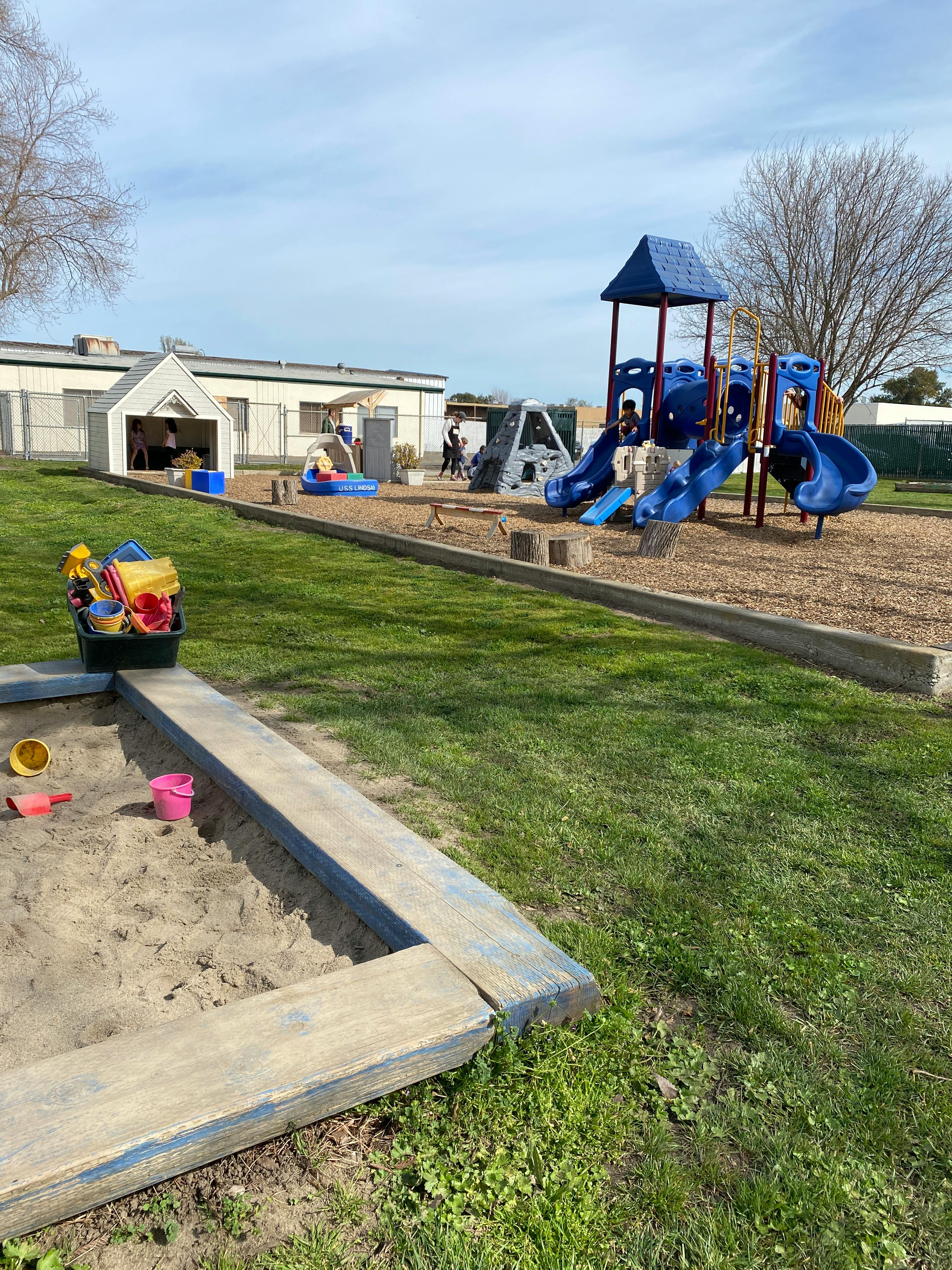 Playground with a sandbox in the foreground and blue play structure in the background